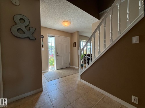 Foyer featuring tile flooring, white front door with sidelight, and staircase with white balusters - 5604 57 Avenue, Beaumont, AB 