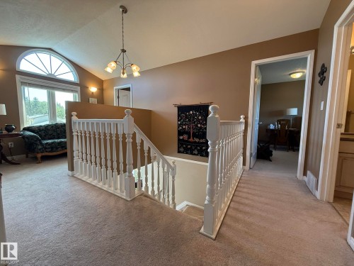 Carpeted upper landing featuring white balustrade railings, a vaulted ceiling, and an arched transom window - 5604 57 Avenue, Beaumont, AB 
