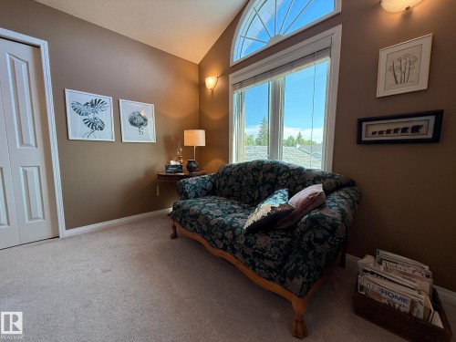 Room featuring a vaulted ceiling with an arched transom window, a large rectangular window, light-colored carpeting, and wall-mounted sconces - 5604 57 Avenue, Beaumont, AB 