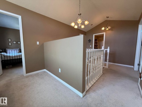Upper-level landing featuring vaulted ceilings with two multi-bulb chandeliers, neutral-toned carpeting, and a painted white balustrade - 5604 57 Avenue, Beaumont, AB 