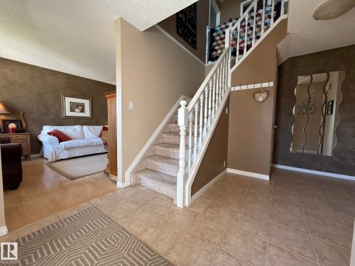 Foyer with tile flooring, leading to a carpeted staircase with white railings, and wood-finish flooring in the adjacent living area - 5604 57 Avenue, Beaumont, AB 