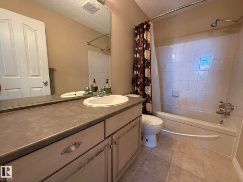 Bathroom featuring a single vanity with an integrated sink, a rectangular mirror, a bathtub with a shower, and light-toned floor tiling - 5604 57 Avenue, Beaumont, AB 