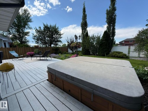 Expansive wood-finish deck featuring a built-in outdoor spa, a dedicated seating area, a manicured lawn, and mature trees - 5604 57 Avenue, Beaumont, AB 