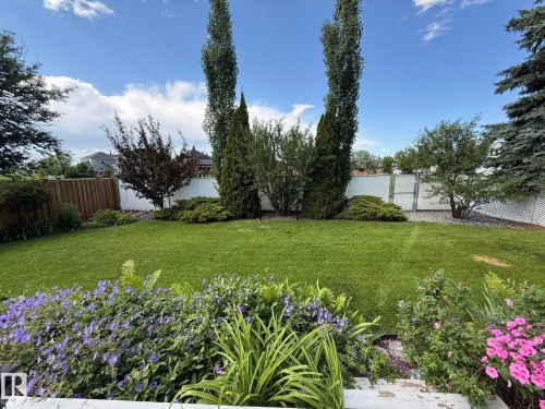 Expansive backyard featuring a manicured lawn, established garden beds with purple and pink flowering plants, and mature perimeter trees - 5604 57 Avenue, Beaumont, AB 