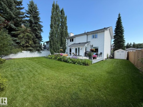 Expansive backyard featuring a lush lawn, white vinyl siding, a rear deck, established perimeter landscaping, and a storage shed - 5604 57 Avenue, Beaumont, AB 