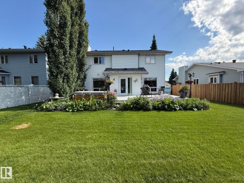 Expansive backyard featuring a manicured lawn, a large deck with an integrated hot tub, and mature perimeter landscaping - 5604 57 Avenue, Beaumont, AB 