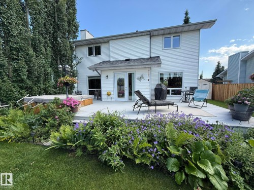 Expansive rear deck featuring a hot tub, direct house access via a double glass door, and surrounding mature landscaping - 5604 57 Avenue, Beaumont, AB 