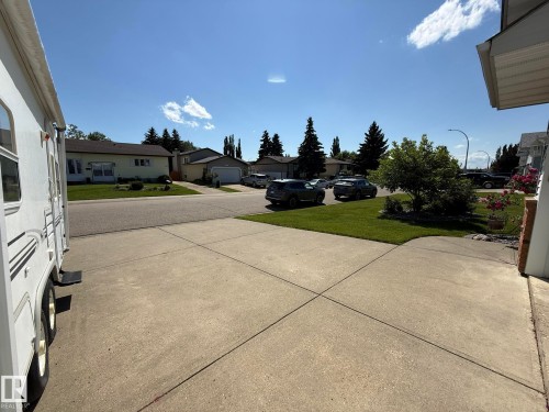 Concrete driveway with a direct street entrance, featuring a manicured lawn and mature trees - 5604 57 Avenue, Beaumont, AB 