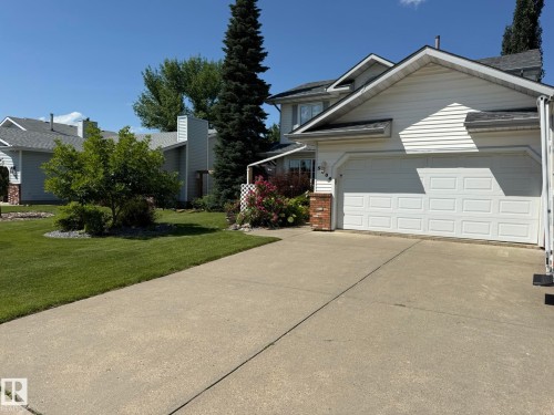 Exterior showcasing a two-car garage, concrete driveway, and front lawn with established landscaping - 5604 57 Avenue, Beaumont, AB 