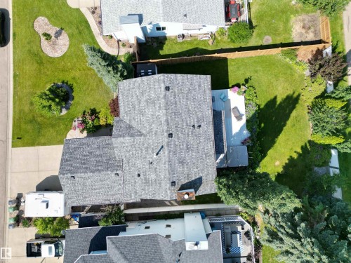 Overhead perspective of a residential property featuring a shingled roof, extensive green lawn, concrete patio, and established perimeter fencing - 5604 57 Avenue, Beaumont, AB 