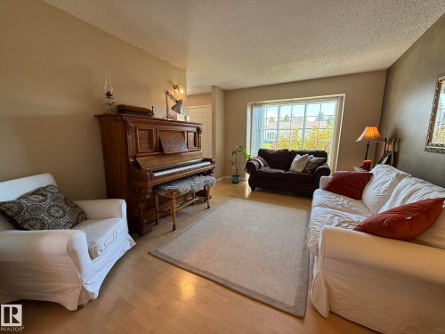 Spacious living area featuring wood-finish flooring, a large picture window, and neutral wall tones - 5604 57 Avenue, Beaumont, AB 