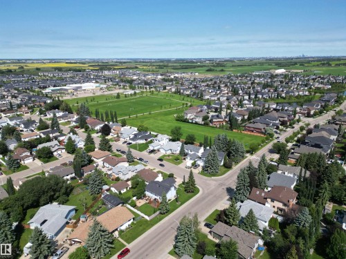 Aerial perspective showcasing a residential area featuring detached homes with varied rooflines and mature landscaping, bordered by expansive green spaces and paved streets - 5604 57 Avenue, Beaumont, AB 