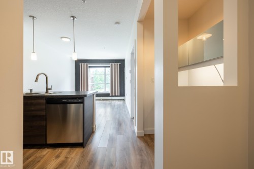 Kitchen island featuring a stainless steel dishwasher, undermount sink with a gooseneck faucet, and two pendant lights - #215 2590 Anderson Wy Sw, Edmonton, AB - Indoor
