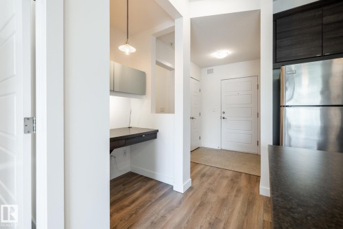 Entryway featuring wood-finish flooring, a built-in desk with overhead cabinetry, stainless steel refrigerator, and dark wood-finish cabinetry - #215 2590 Anderson Wy Sw, Edmonton, AB - Indoor Photo Showing Other Room