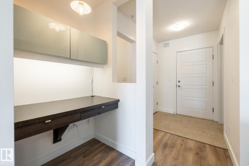 Dedicated workstation with a floating dark wood-finish desk, under-cabinet lighting, and overhead storage cabinetry - #215 2590 Anderson Wy Sw, Edmonton, AB - Indoor Photo Showing Other Room