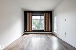 Spacious room featuring wood-finish flooring, a large window with exterior scenery, a glass-paneled door, baseboard heating, and a textured accent wall - 