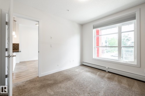 Light-filled room featuring a large window with roller shade, neutral plush carpeting, and white baseboards - #215 2590 Anderson Wy Sw, Edmonton, AB - Indoor Photo Showing Other Room