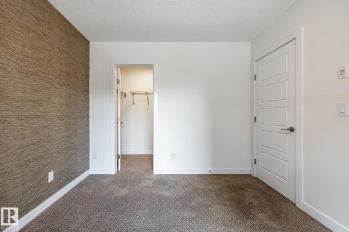Plush carpeted flooring complementing a textured accent wall - #215 2590 Anderson Wy Sw, Edmonton, AB - Indoor Photo Showing Other Room