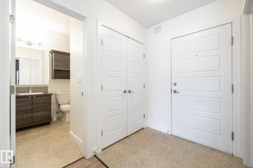 Entryway featuring a white paneled door with brushed nickel hardware, closet with bi-fold doors, and neutral-toned flooring - #215 2590 Anderson Wy Sw, Edmonton, AB - Indoor Photo Showing Other Room