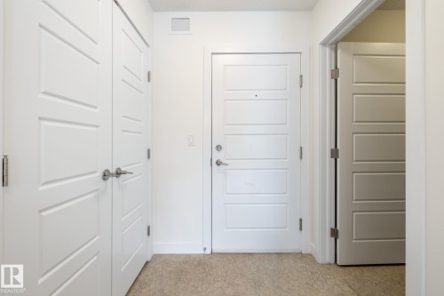 Entryway featuring light-colored flooring, white paneled doors with brushed nickel hardware, and white baseboards - #215 2590 Anderson Wy Sw, Edmonton, AB - Indoor Photo Showing Other Room