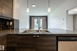 Kitchen featuring a dual-basin stainless steel sink with a high-arc faucet, dark wood-finish cabinetry, a black subway tile backsplash, and dark countertops - 