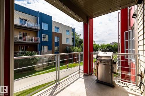 Spacious private balcony featuring a concrete floor, glass and metal railing, and a red accent column - #215 2590 Anderson Wy Sw, Edmonton, AB - Outdoor