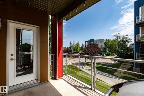 Balcony featuring a glass panel railing, textured flooring, and a full-light exterior door - #215 2590 Anderson Wy Sw, Edmonton, AB - Outdoor With Exterior