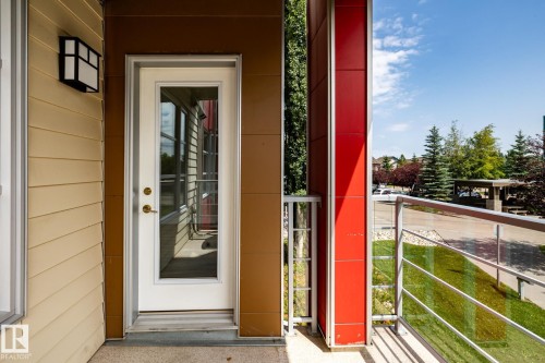 Private balcony featuring a glass panel railing, red exterior accent panels, and a full-light glass door - #215 2590 Anderson Wy Sw, Edmonton, AB - Outdoor With Exterior