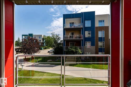 Balcony with glass and metal railing, overlooking a landscaped courtyard with green space and mature trees - #215 2590 Anderson Wy Sw, Edmonton, AB - Outdoor