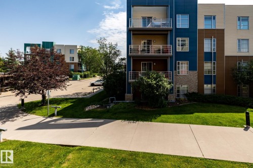 Contemporary multi-story building featuring blue and beige siding with stone accents - #215 2590 Anderson Wy Sw, Edmonton, AB - Outdoor With Facade