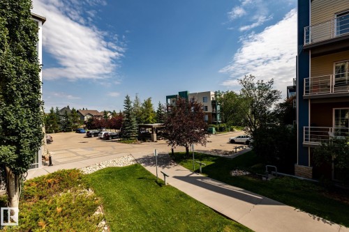Articulated pavement parking area bordered by landscaped grounds featuring mature trees and shrubs - #215 2590 Anderson Wy Sw, Edmonton, AB - Outdoor