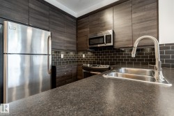 Kitchen featuring dark wood-finish cabinetry, stainless steel appliances, black subway tile backsplash, a dual basin stainless steel sink, and dark flecked countertops - 