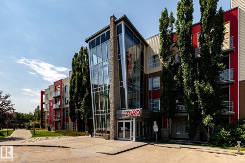 Contemporary multi-story building featuring a prominent glass and brick facade entrance - #215 2590 Anderson Wy Sw, Edmonton, AB - Outdoor With Facade