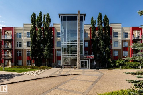 Contemporary multi-story building featuring a prominent glass-enclosed central entrance - #215 2590 Anderson Wy Sw, Edmonton, AB - Outdoor With Facade