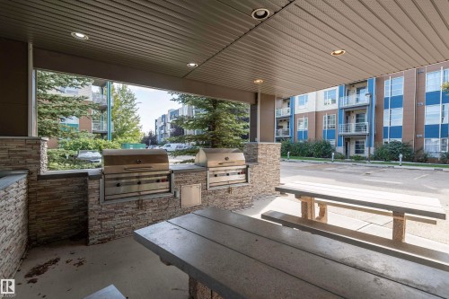Covered outdoor grilling station featuring two built-in stainless steel grills and stone-finish surrounds - #215 2590 Anderson Wy Sw, Edmonton, AB - Outdoor With Deck Patio Veranda