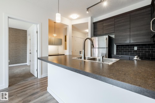 Kitchen island featuring a double basin stainless steel sink with a gooseneck faucet - #215 2590 Anderson Wy Sw, Edmonton, AB - Indoor Photo Showing Kitchen With Double Sink With Upgraded Kitchen
