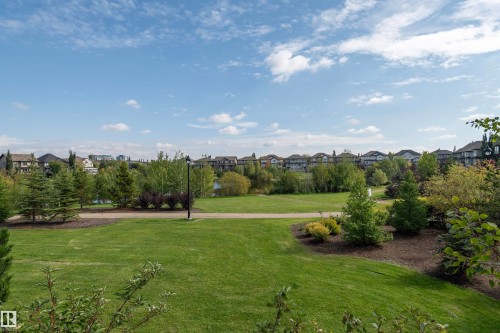 Expansive green space featuring mature trees, a paved walking path, and a body of water with a fountain - #215 2590 Anderson Wy Sw, Edmonton, AB - Outdoor With View