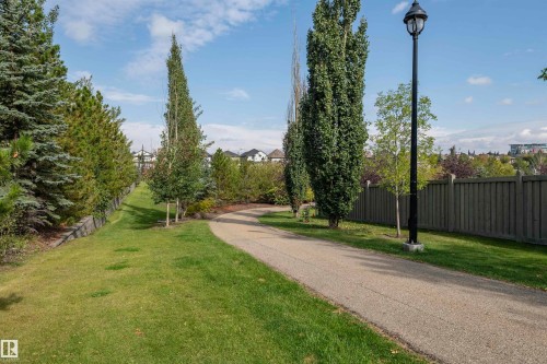 Paved pathway bordered by mature trees and manicured lawn - #215 2590 Anderson Wy Sw, Edmonton, AB - Outdoor