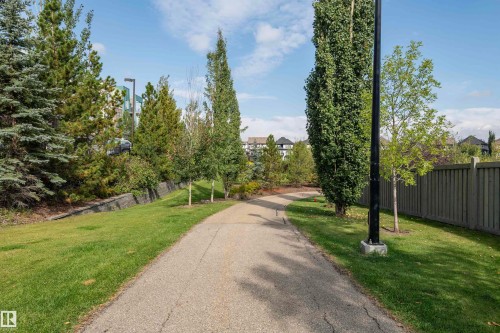 Paved pathway bordered by mature trees and manicured lawns - #215 2590 Anderson Wy Sw, Edmonton, AB - Outdoor