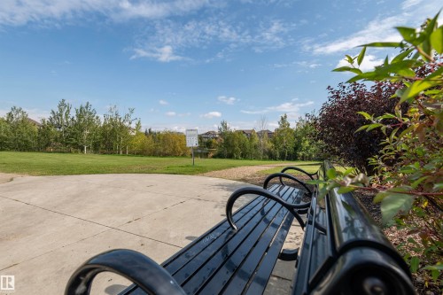 Paved pathway with a black slatted park bench - #215 2590 Anderson Wy Sw, Edmonton, AB - Outdoor