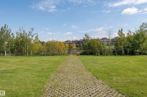 Expansive grassy area with a permeable paver path leading towards a tranquil body of water - #215 2590 Anderson Wy Sw, Edmonton, AB - Outdoor With View