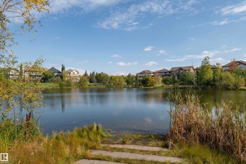 Lakeside residential setting with mature trees and natural vegetation bordering the water - #215 2590 Anderson Wy Sw, Edmonton, AB - Outdoor With Body Of Water With View