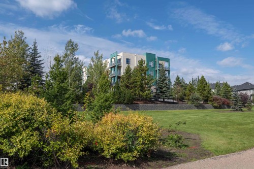 Contemporary building exterior featuring light-colored siding and teal-paneled accents - #215 2590 Anderson Wy Sw, Edmonton, AB - Outdoor