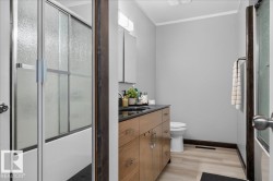 Bathroom featuring a light wood-finish vanity with a dark countertop, dual sinks, and light gray walls - 