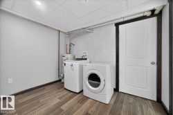 Utility area featuring wood-finish flooring, white paneled door with dark trim, and a drop ceiling with recessed lighting - 