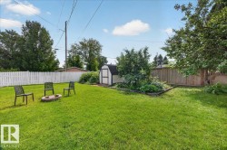 Expansive backyard featuring a green lawn, a white picket fence, a wooden privacy fence, a fire pit area, and a storage shed - 