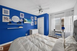 Bedroom featuring rich blue accent wall, wood-finish flooring, a ceiling fan with integrated lighting, and a double-panel closet with white bi-fold doors - 
