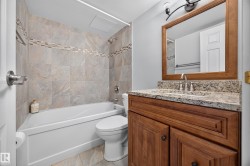 Bathroom featuring a wood-finish vanity with a stone countertop, an integrated sink, and a framed mirror - 
