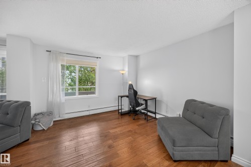 Spacious room featuring wood-finish flooring, a large window with natural light, white walls, and white baseboards - #602 9725 106 St Nw, Edmonton, AB 
