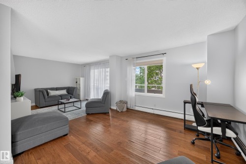 Spacious living area featuring rich wood-finish flooring, ample natural light from a large window, a sliding glass door, and neutral wall tones - #602 9725 106 St Nw, Edmonton, AB 